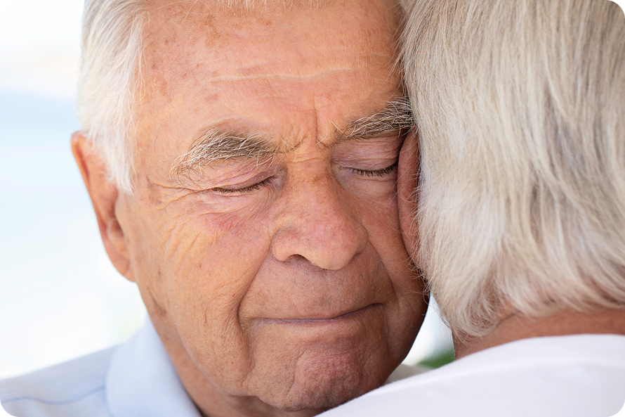 A close-up of a senior man with his eyes closed, embracing another person.