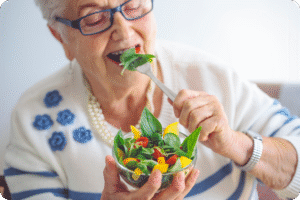 A senior woman with glasses enjoys a fresh salad.
