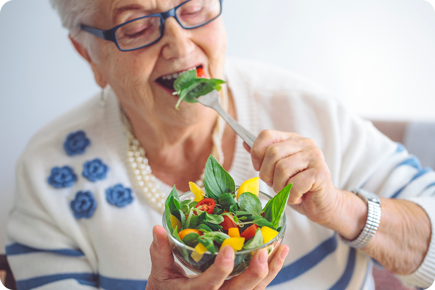 A senior woman with glasses enjoys a fresh salad.