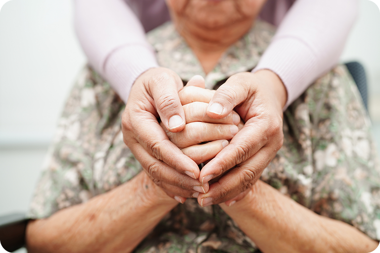 A close-up of a caregiver's hands holding the clasped hands of a senior person.