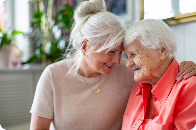A happy, middle-aged woman and a senior woman smile at each other while touching foreheads.