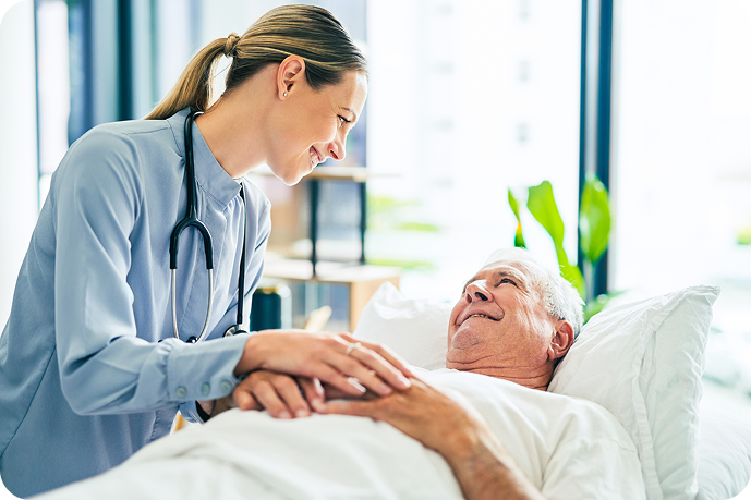 A friendly nurse with a stethoscope gently touches the chest of a smiling senior man lying in a hospital bed.