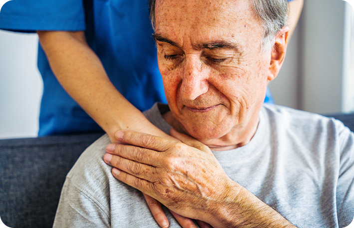 A close-up shot of a caregiver's hand gently resting on the shoulder of a pensive senior man.