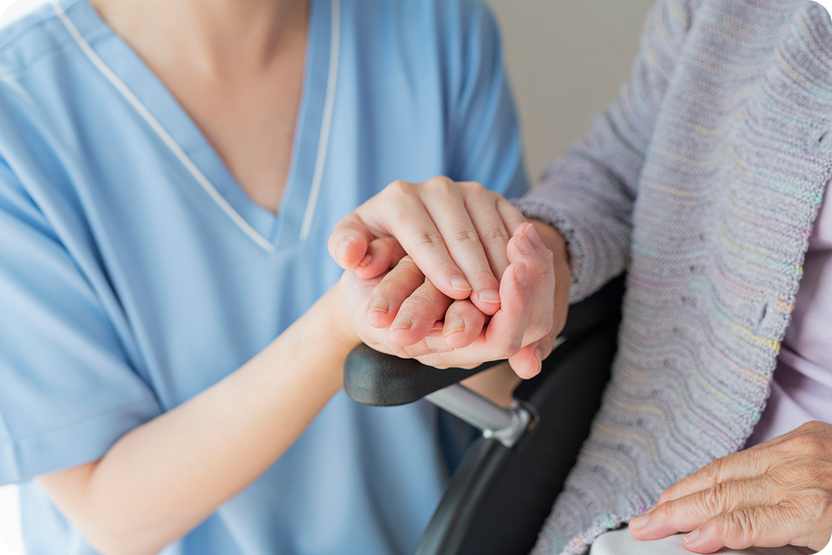 A close-up of a young caregiver's hands gently holding the hands of an elderly person, providing reassurance and care.