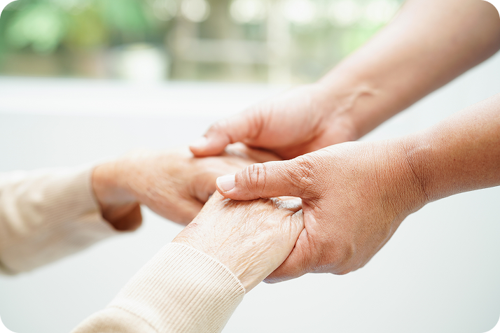 A close-up shot of a younger person's hands gently holding the hands of an elderly person, showing care and support.