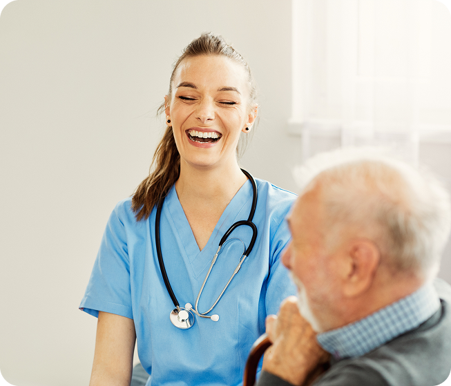 A cheerful female caregiver with a stethoscope laughs with a senior man holding a cane.