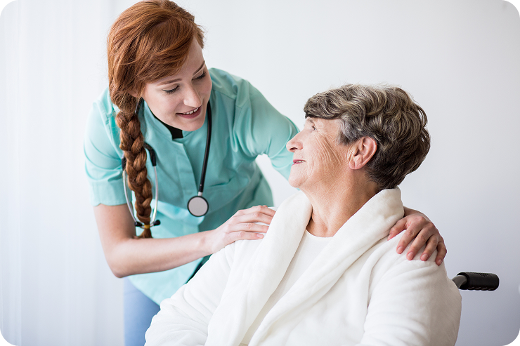A caring female caregiver puts her hands on the shoulders of a senior woman in a wheelchair.