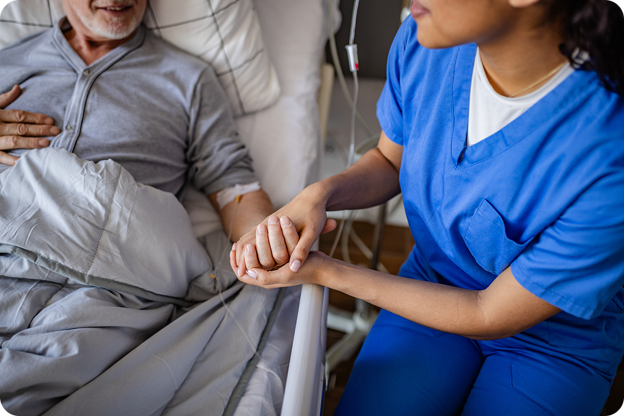 A healthcare worker holds the hand of a patient in a hospital bed, conveying comfort and support during treatment.