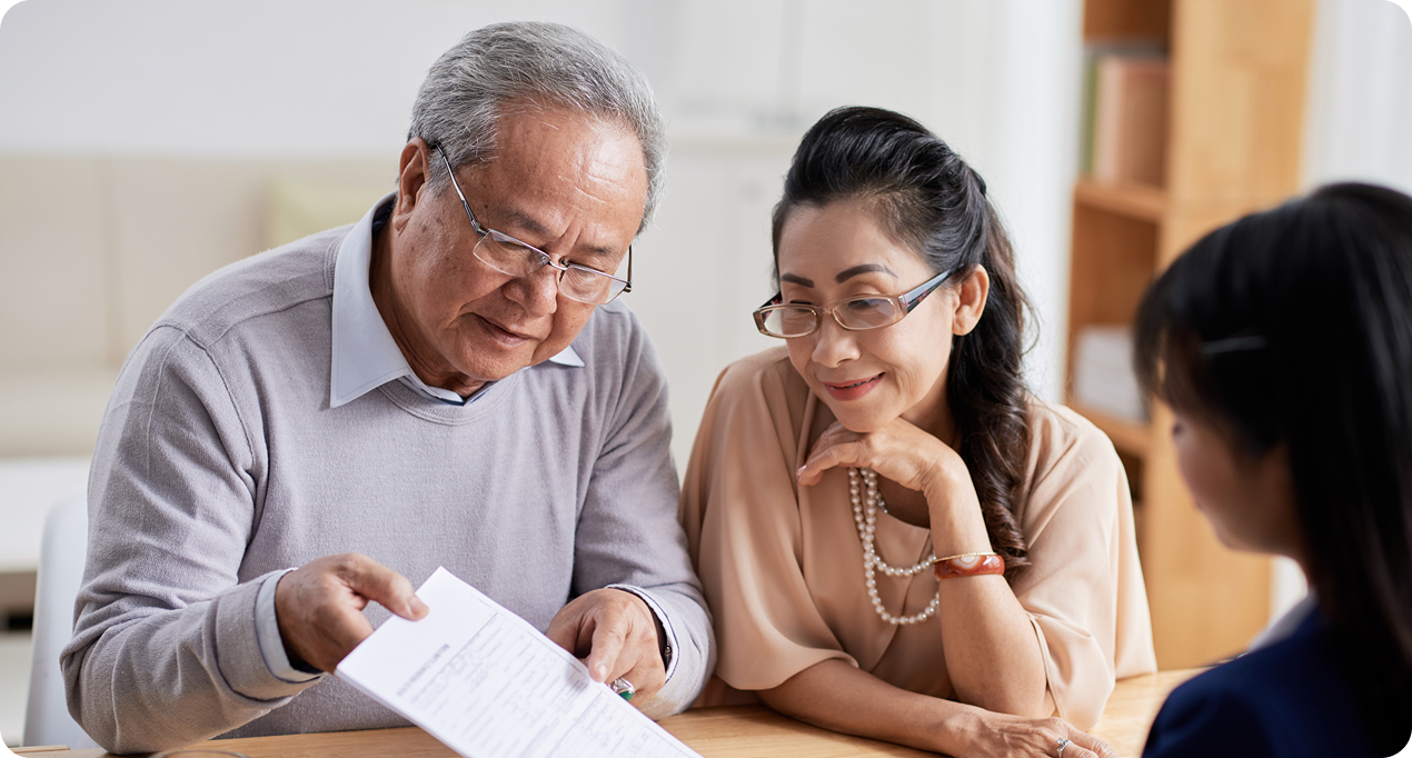 An elderly man and woman attentively discuss documents with a younger female professional in a modern office setting.