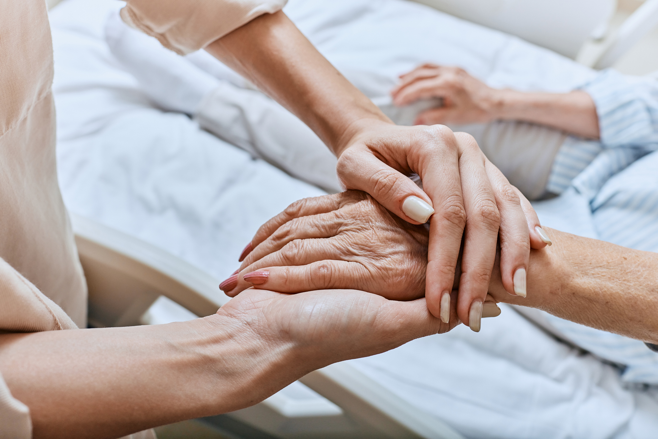 Hands of a caregiver gently hold an elderly patient's hand in a hospital bed, conveying compassion and support.