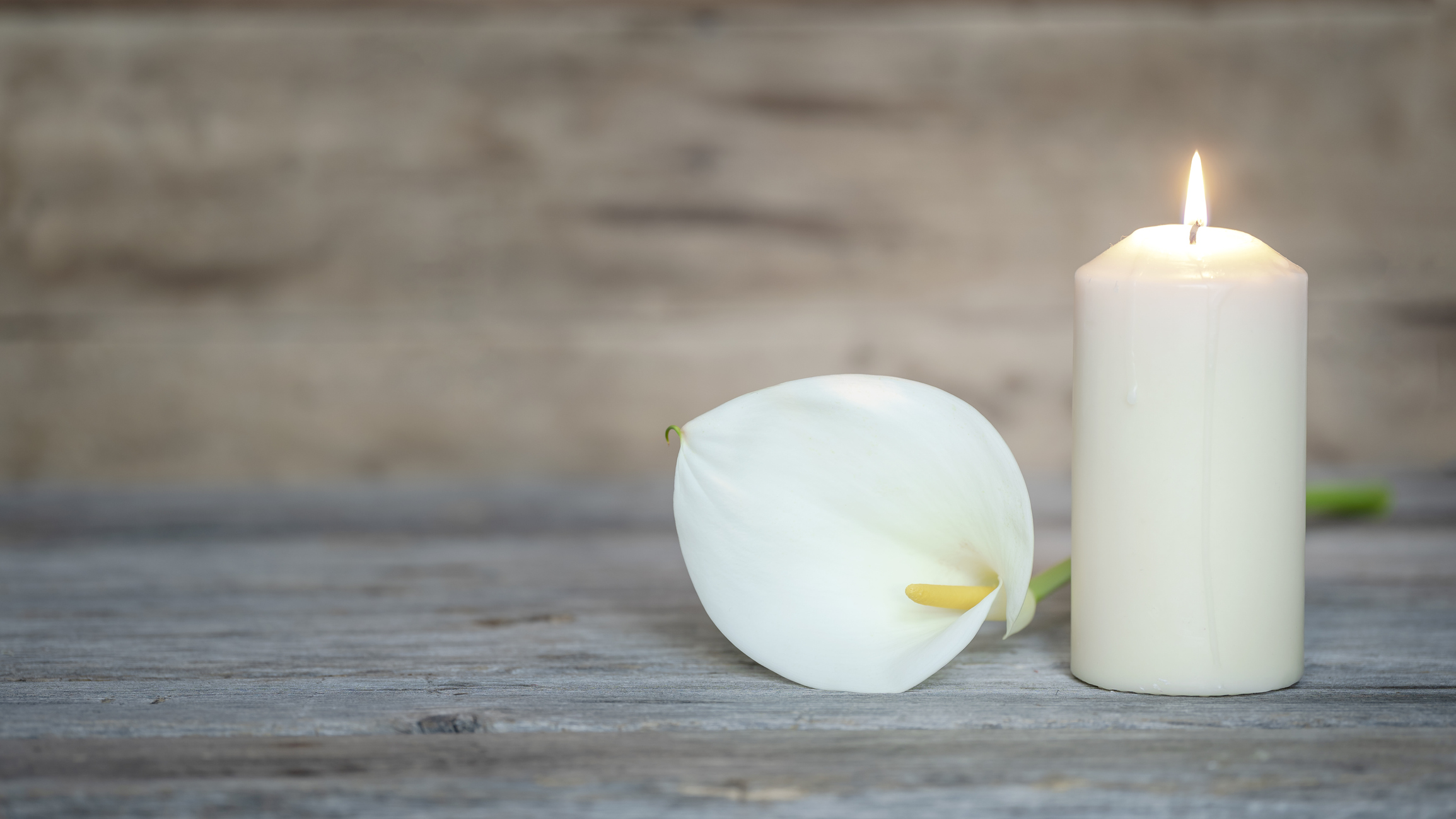 White calla flower next to a lighted candle on wooden background.
