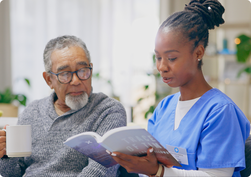 A healthcare worker discusses a book titled with an older man while he enjoys a warm beverage.