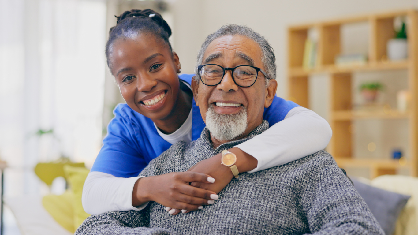 Healthcare professional smiling with an elderly man, both sitting comfortably in a bright, inviting indoor space.