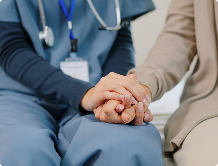 Healthcare professional in scrubs gently holds the hands of a patient in a comforting, supportive interaction.