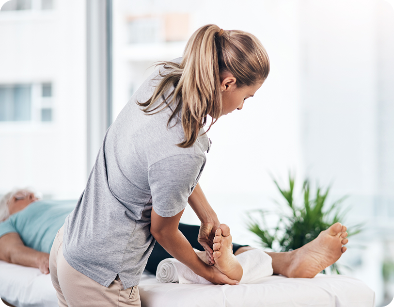 A healthcare professional provides foot therapy to a patient on a treatment table in a bright, modern clinic environment.