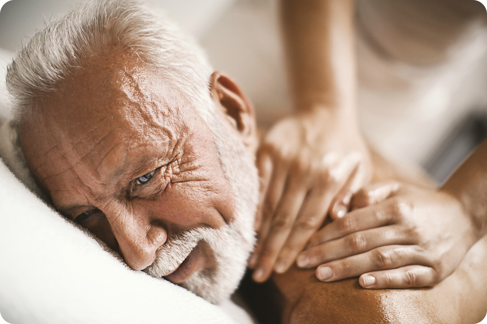 Senior man receiving a massage, showing relaxation and care, while a therapist's hands are gently placed on his shoulder.