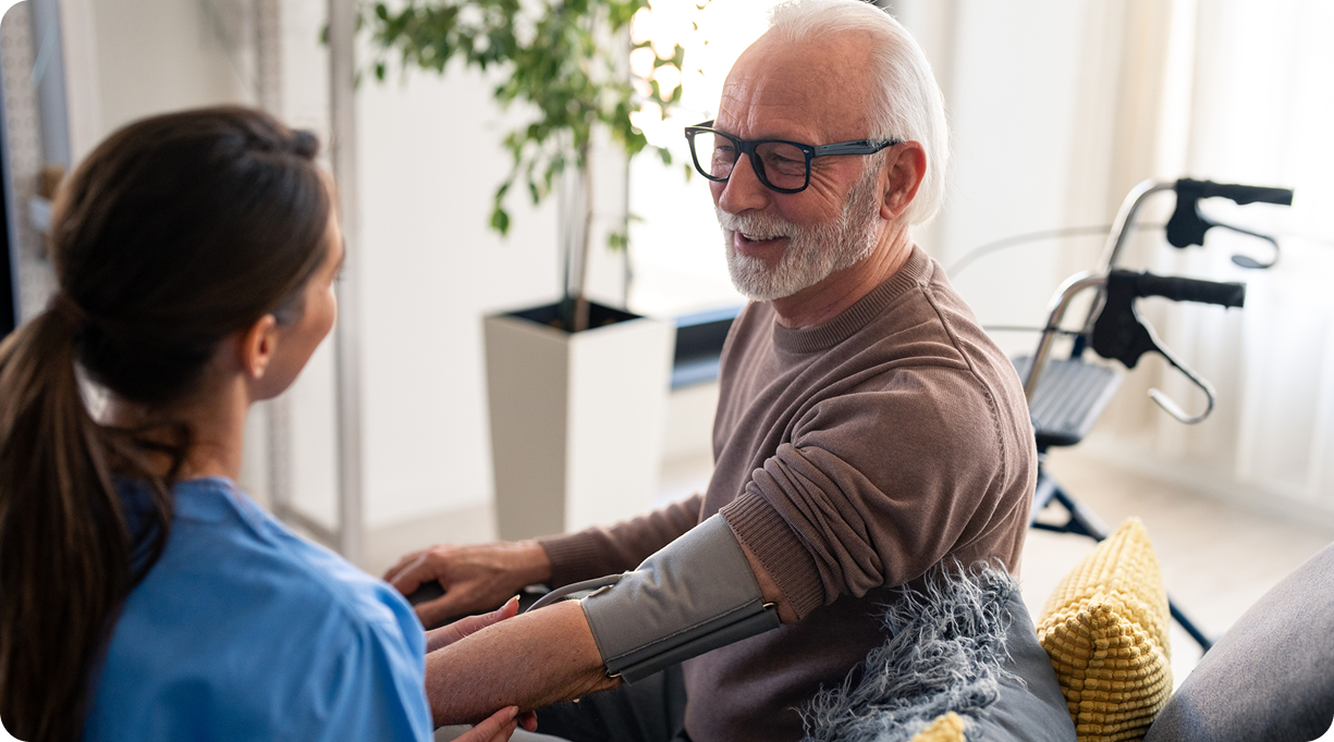 A happy male caregiver helps a smiling senior man with his blood pressure cuff at home.