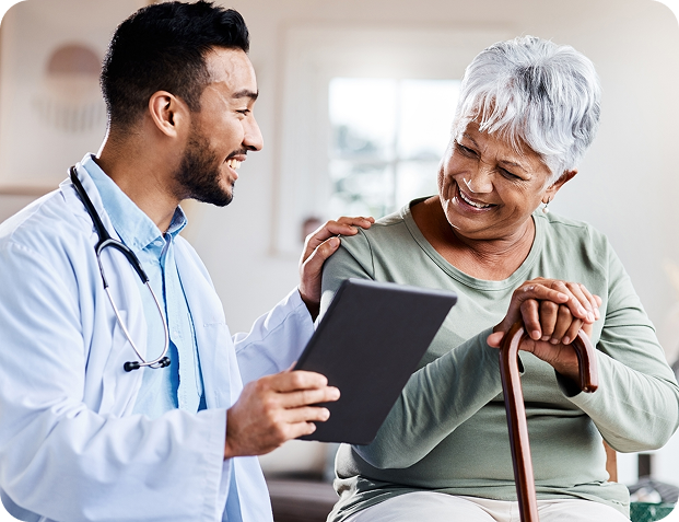 A friendly doctor shows a tablet to a smiling senior woman holding a walking stick.