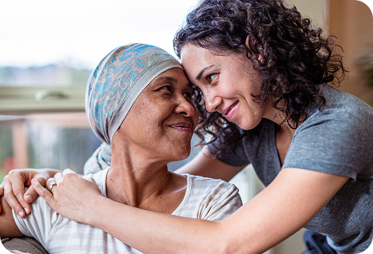 Two women share an affectionate moment indoors, one wearing a headscarf, sitting close together with warm expressions.