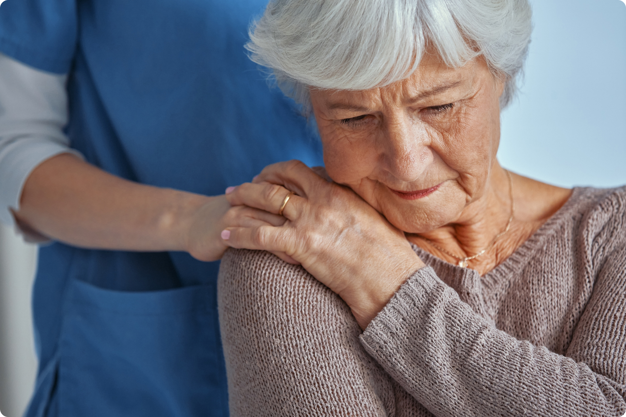 A caregiver gently comforts an elderly woman who appears to be in distress, showcasing a compassionate healthcare environment.