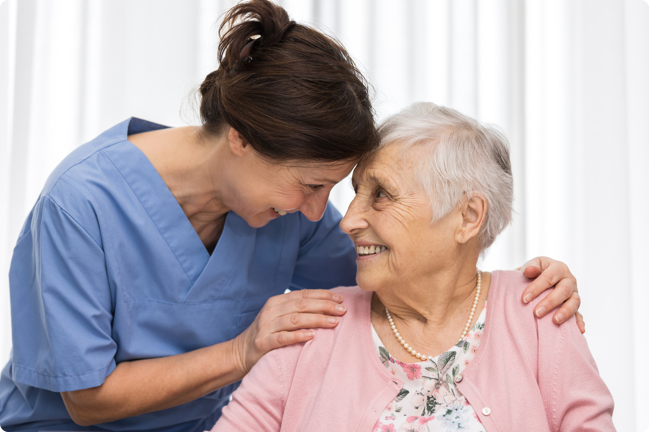 Healthcare worker and elderly woman share a joyful moment, emphasizing compassionate care in a bright, welcoming environment.