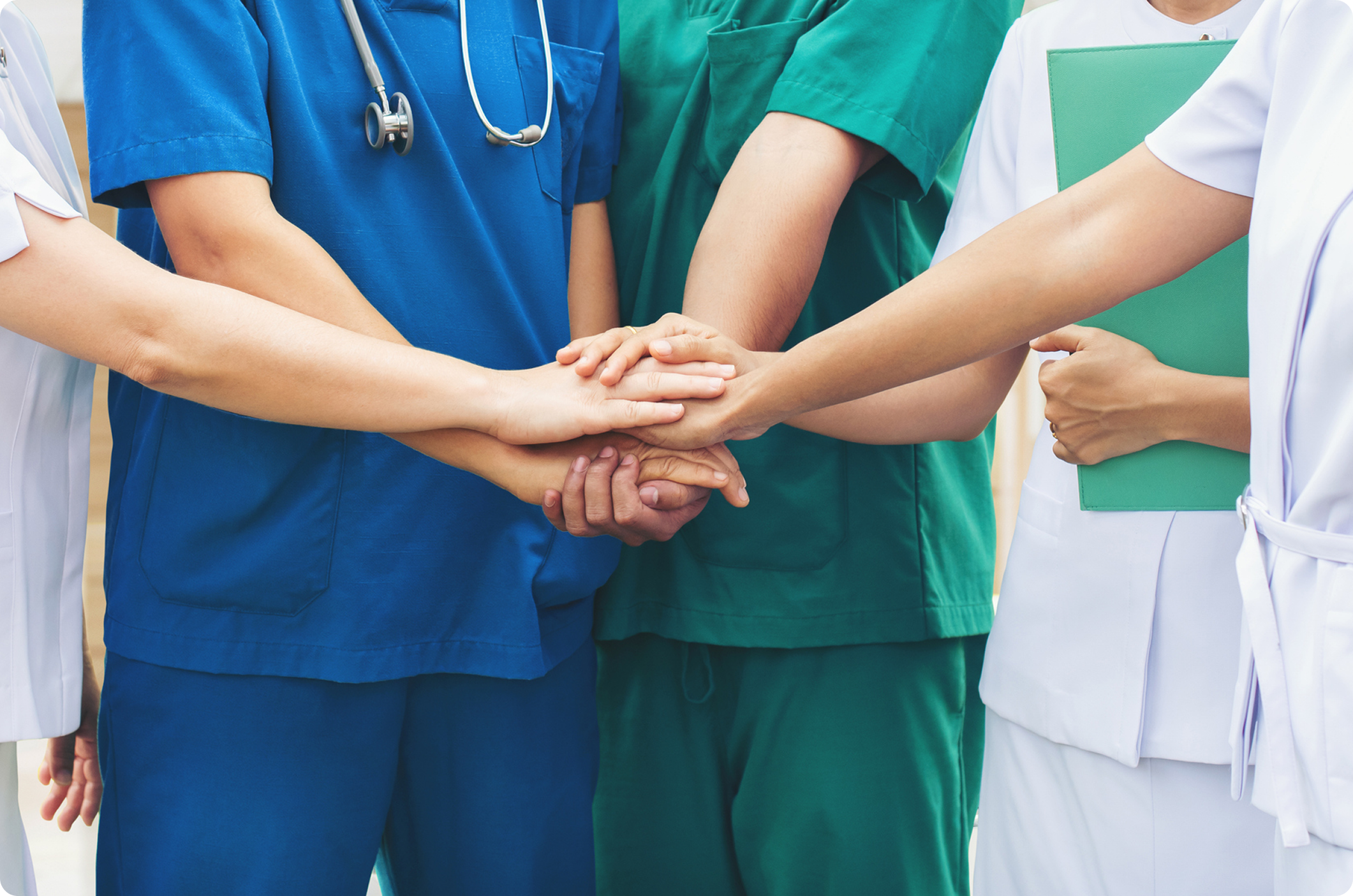 Medical professionals in scrubs and a lab coat joining hands, symbolizing teamwork and collaboration in healthcare.
