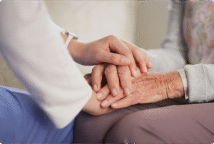 A caregiver gently holds the hands of an elderly person, emphasizing compassion and connection in a warm environment.