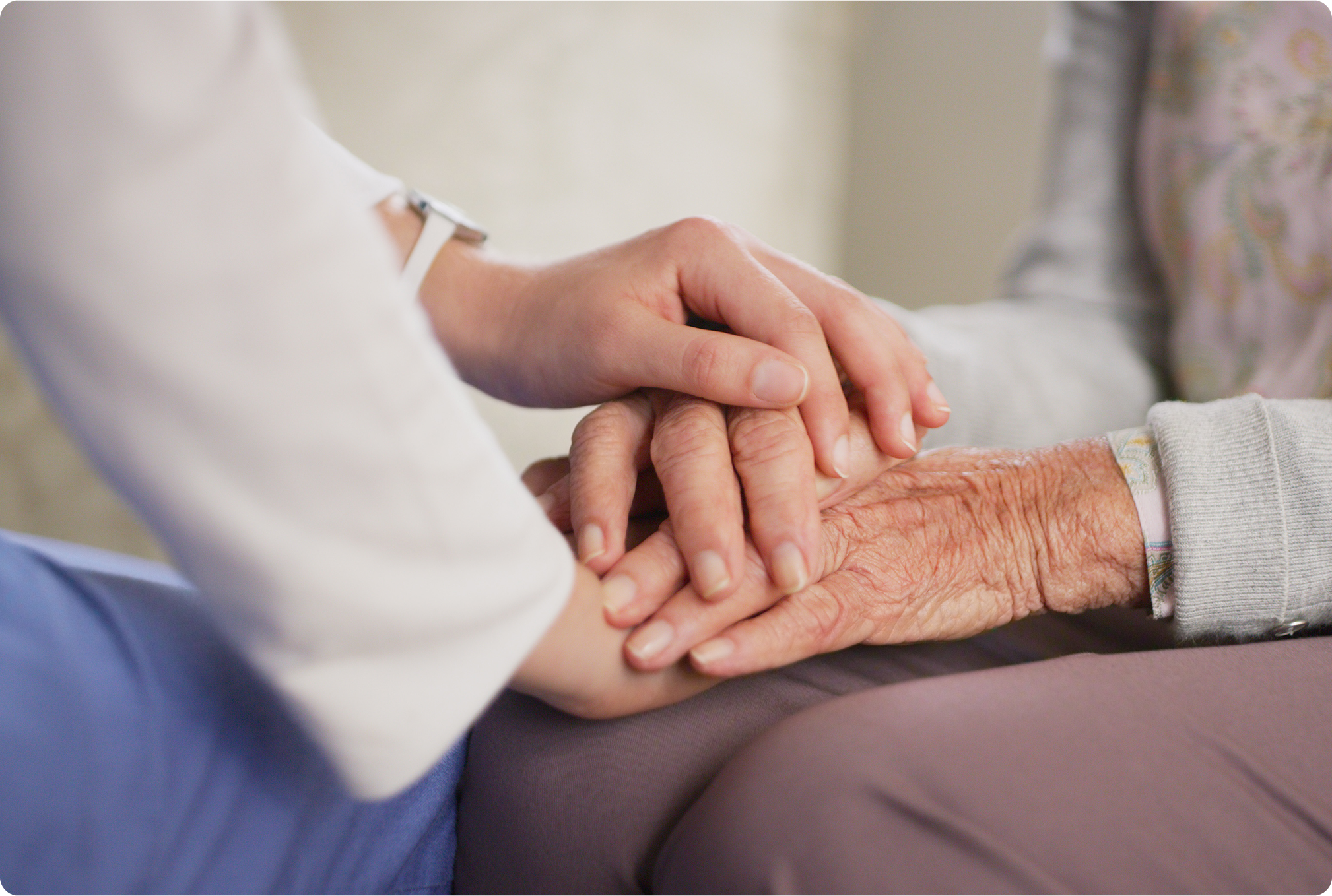 A caregiver gently holds the hands of an elderly person, emphasizing compassion and connection in a warm environment.