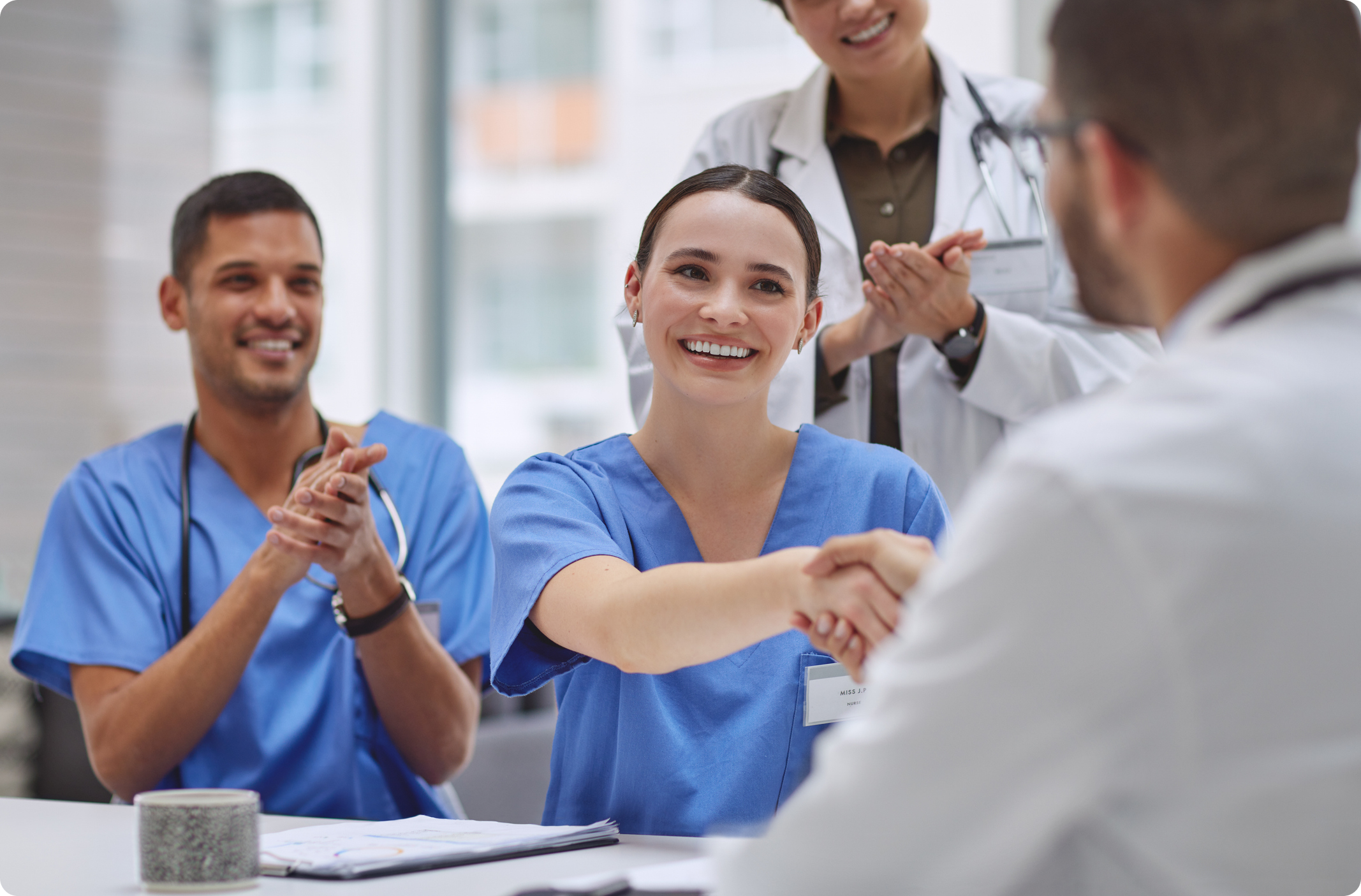 Healthcare professionals in blue scrubs celebrate a successful meeting, with one person shaking hands and smiling.