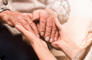 A young hand gently holds the weathered hands of an elderly person, conveying warmth and connection in a serene setting.