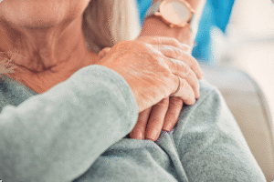 Close-up of two hands, one elderly and aged, resting on the senior's shoulder, highlighting connection