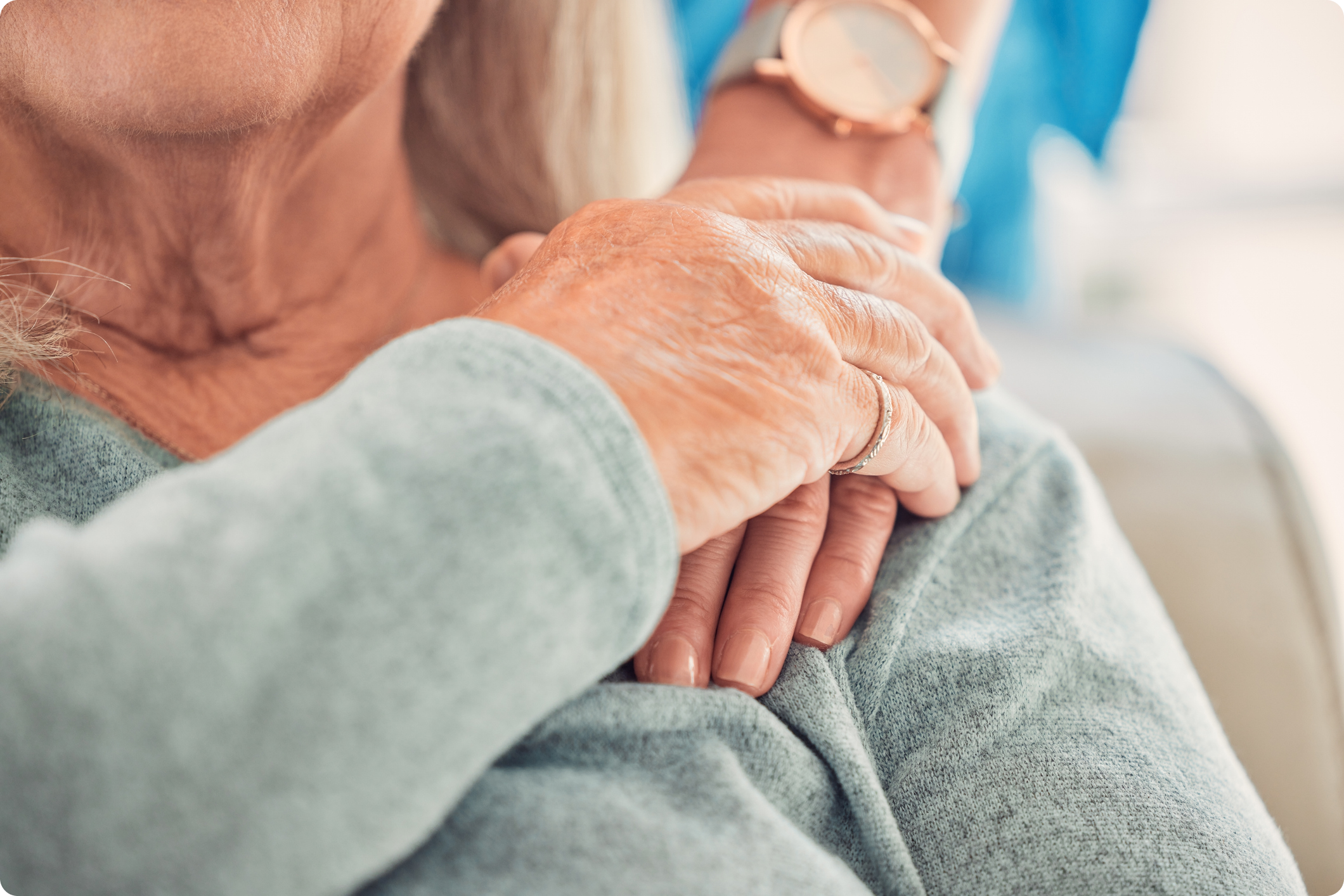 Close-up of two hands, one elderly and aged, resting on the senior's shoulder, highlighting connection
