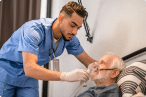 Healthcare professional in blue scrubs adjusting oxygen mask on elderly patient in a home care setting.