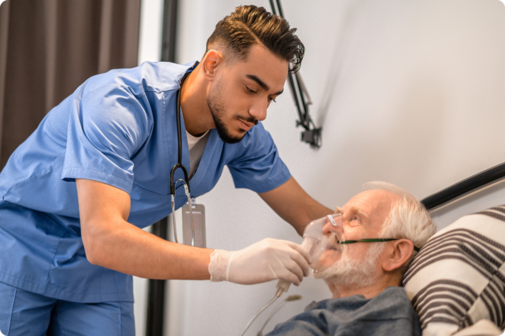 Healthcare professional in blue scrubs adjusting oxygen mask on elderly patient in a home care setting.