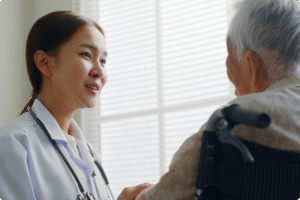 A healthcare professional engages with an elderly patient in a well-lit room with blinds.