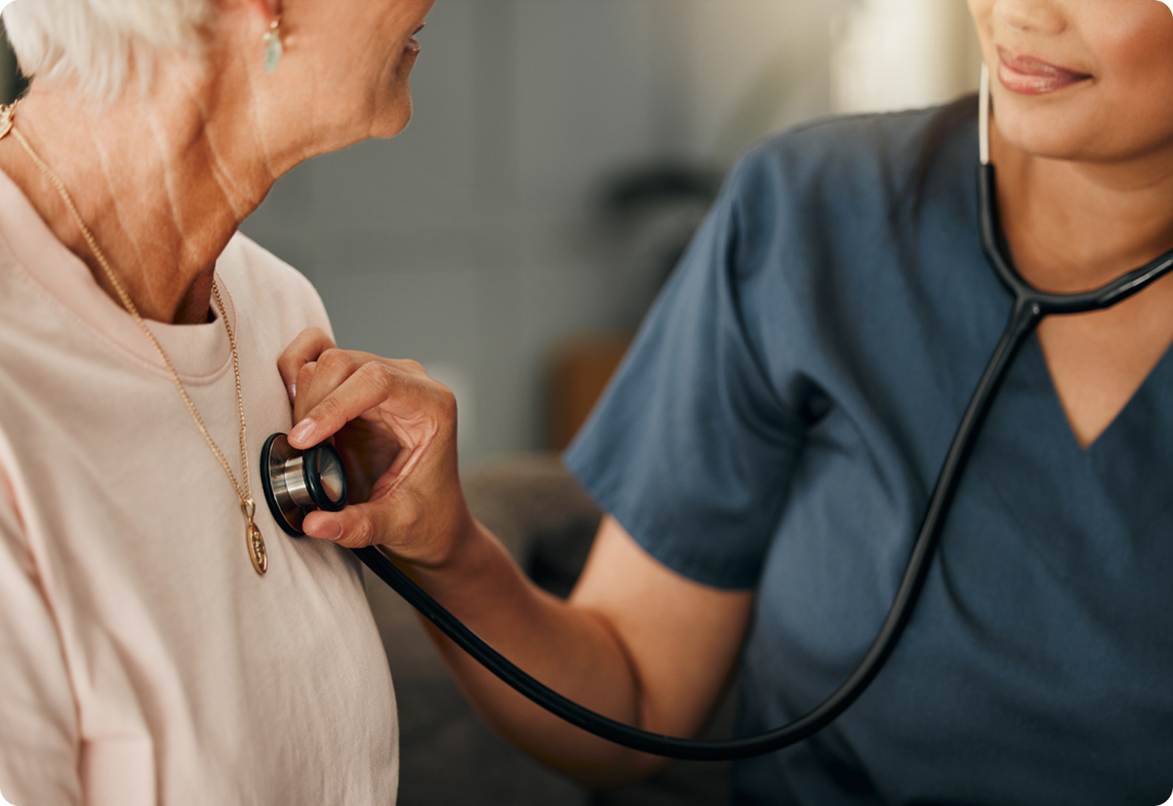 A healthcare professional uses a stethoscope to examine an older woman's chest in a comfortable clinical environment.