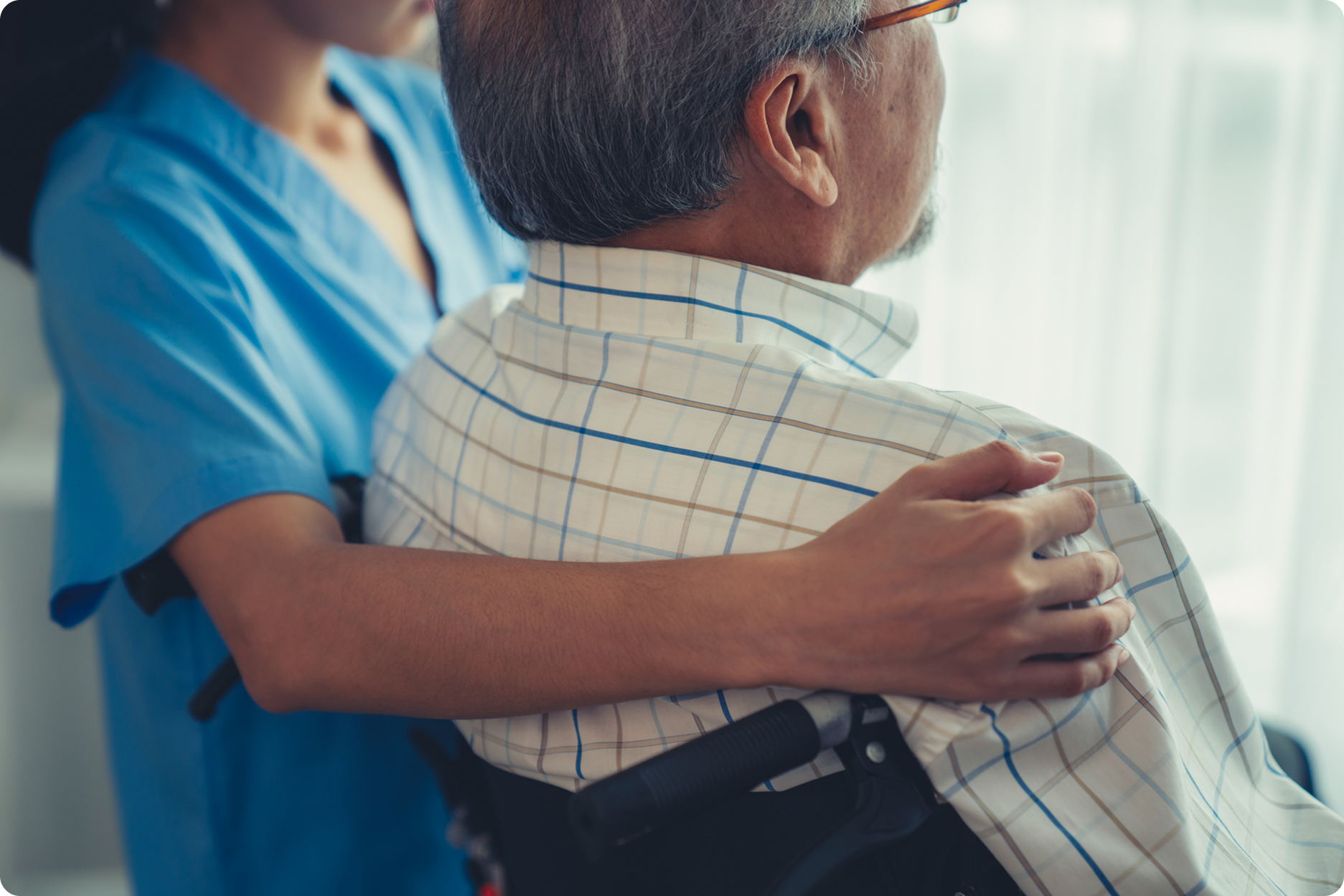 A caregiver gently rests their hand on the shoulder of an elderly man in a wheelchair, highlighting supportive care in a medi