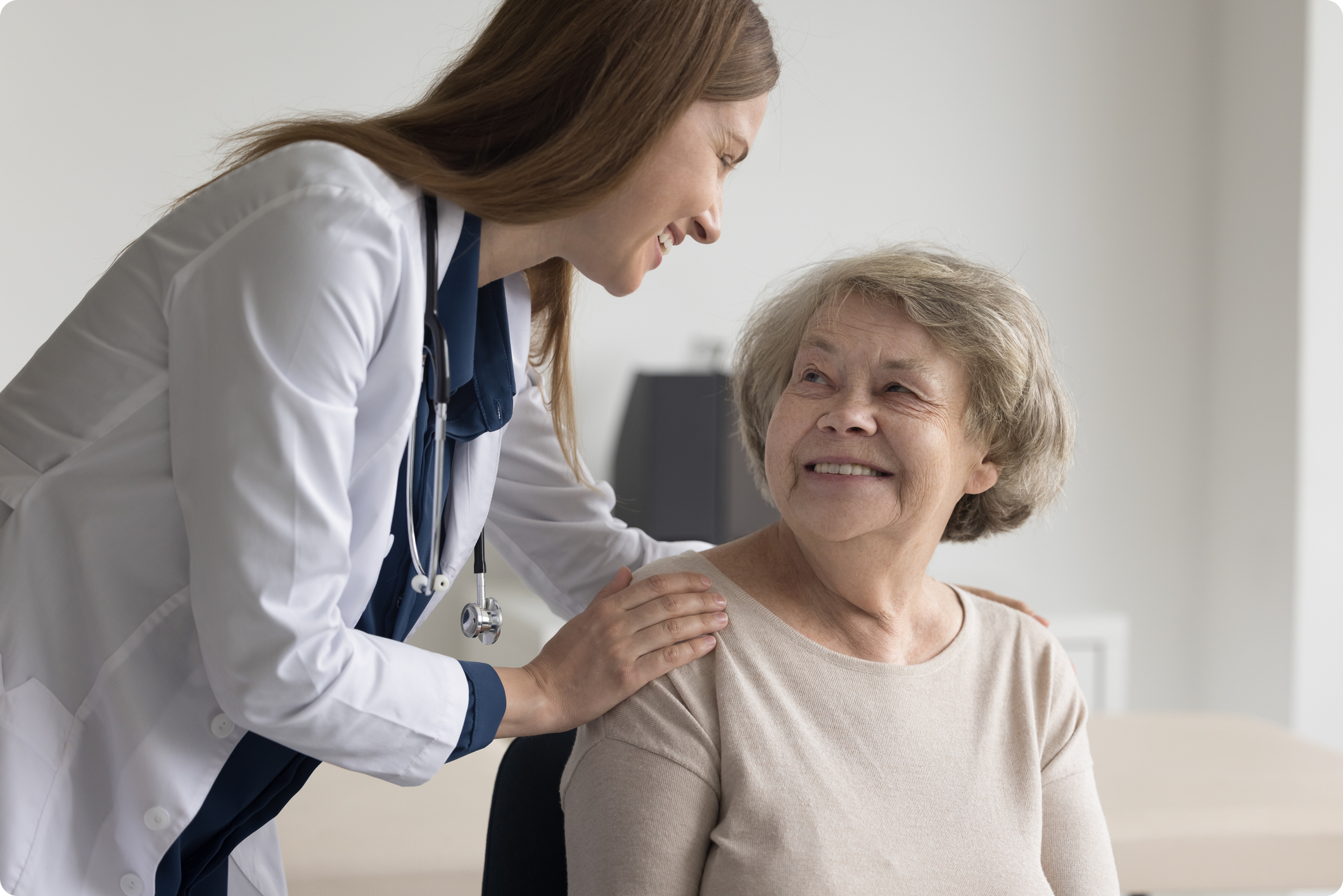 A healthcare provider in a white coat engages positively with an elderly patient during a consultation in an office setting.