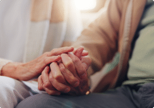 Hands of an elderly couple gently clasped together, symbolizing connection and support in a warm, cozy environment.