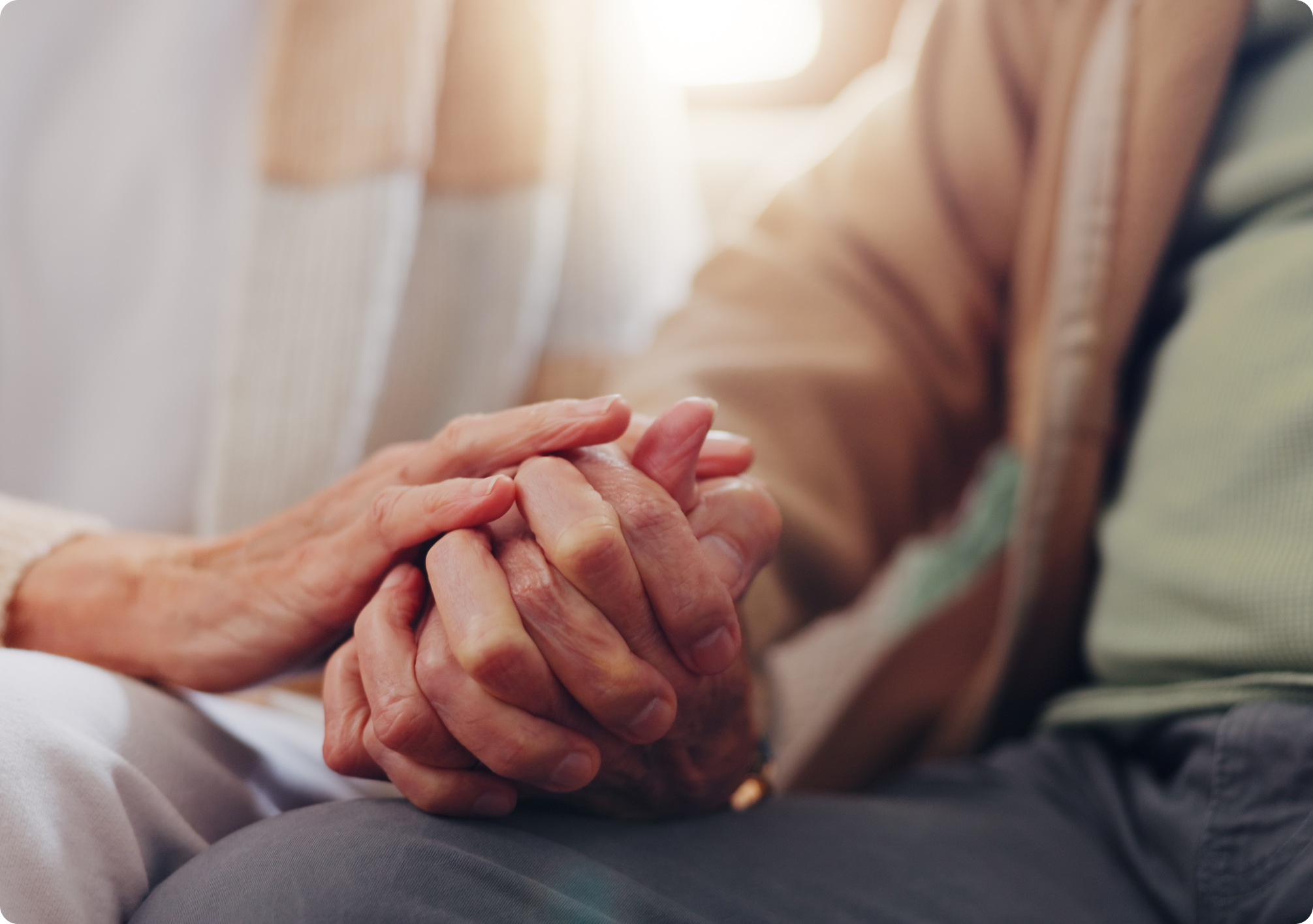 Hands of an elderly couple gently clasped together, symbolizing connection and support in a warm, cozy environment.