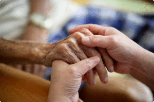 Two hands interlocked, one aged and wrinkled, the other smooth, symbolizing care and connection in a warm environment.