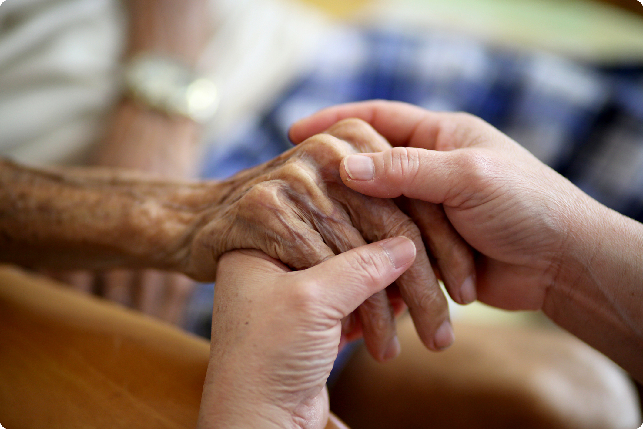 Two hands interlocked, one aged and wrinkled, the other smooth, symbolizing care and connection in a warm environment.