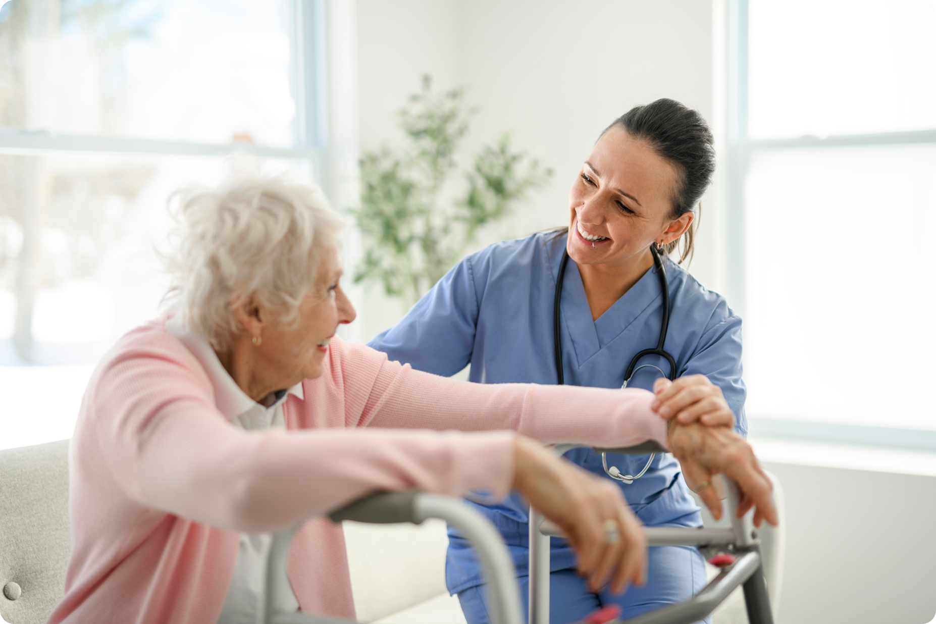 A healthcare professional assists an elderly woman with a walker in a bright, welcoming indoor environment.