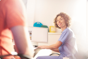Smiling healthcare professional in blue scrubs engaging with a patient in a bright, modern medical office setting.