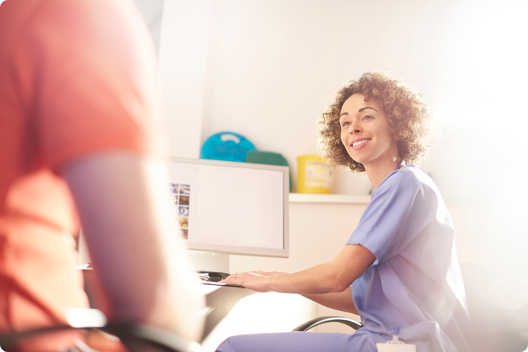 Smiling healthcare professional in blue scrubs engaging with a patient in a bright, modern medical office setting.