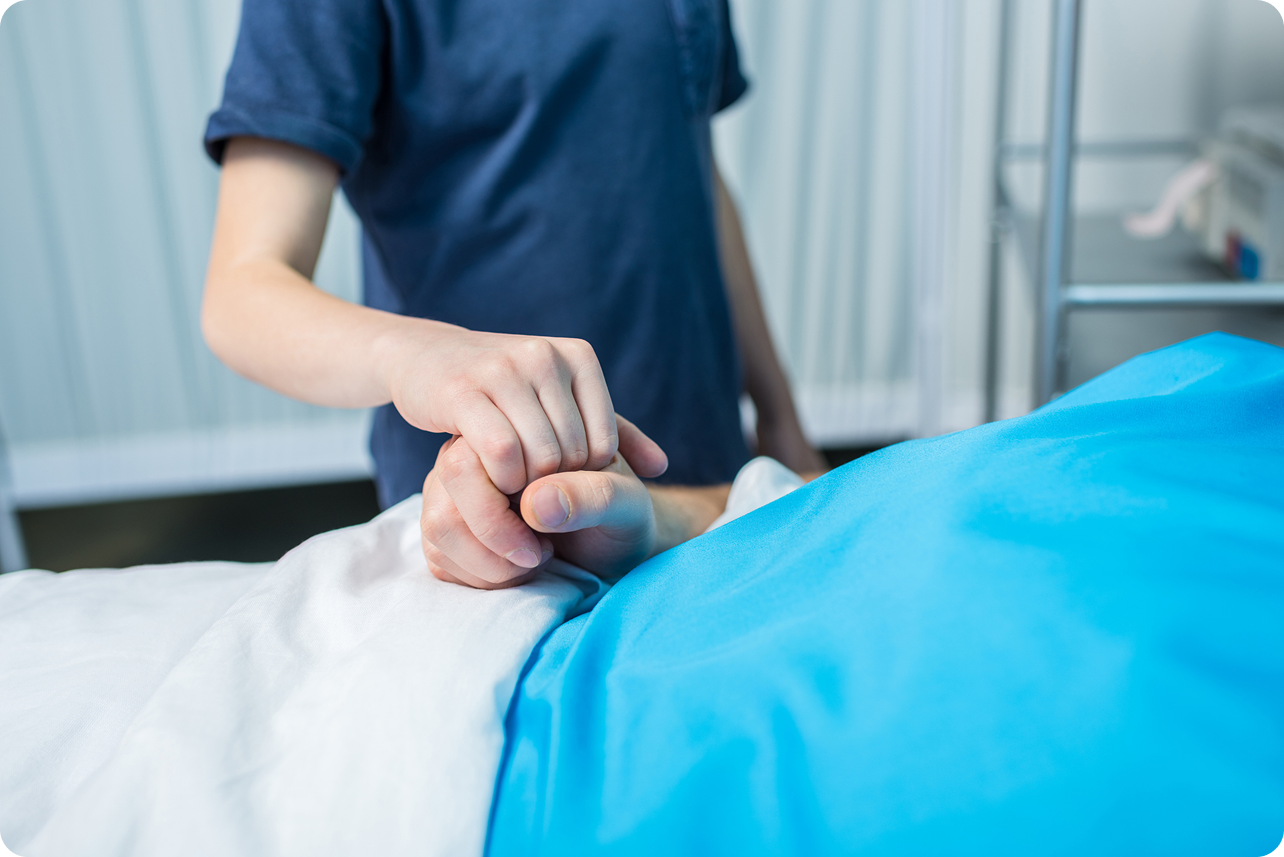 A child's hand holds an adult's hand while resting on a hospital bed covered with a blue and white blanket.
