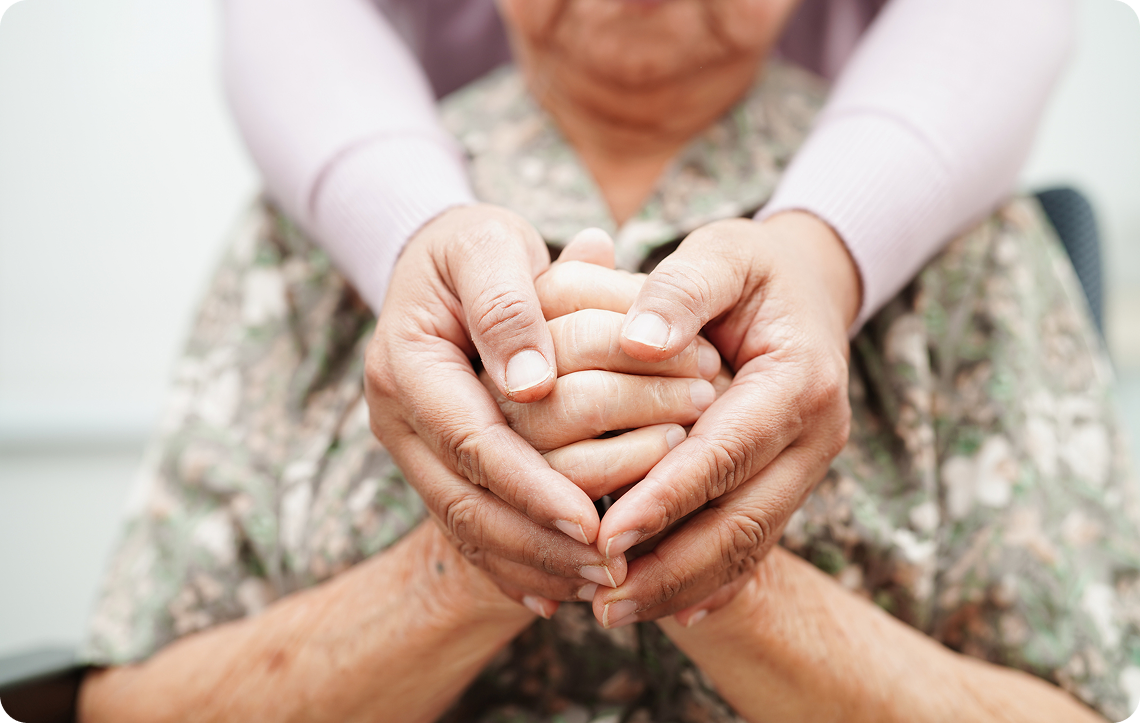 Two hands one elderly and one younger delicately clasp each other in a warm, supportive gesture, conveying care and connection.