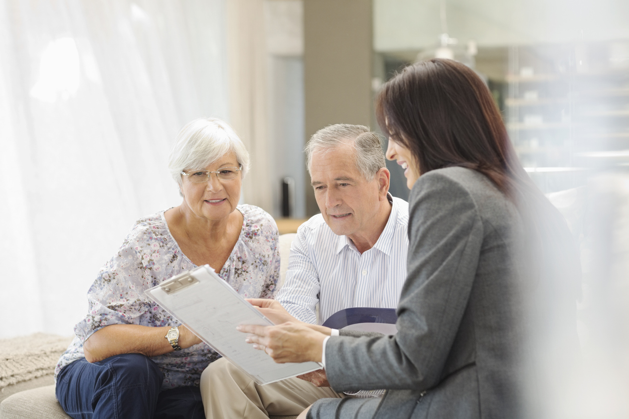 A senior couple discusses important information with a professional, reviewing a clipboard in a comfortable indoor setting.